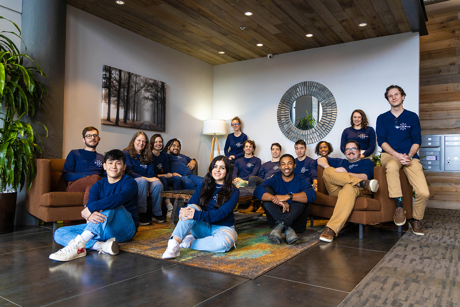 Photo of a young group of people sitting on brown couches in an office room with white walls and brown floors.