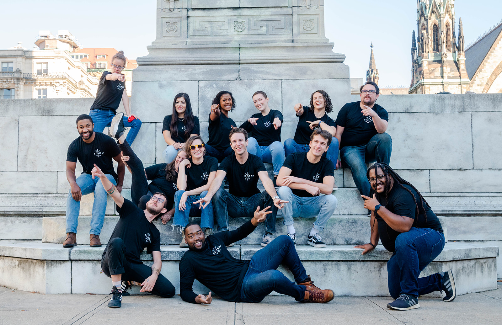 A group of young people sitting at the base of a white marble monument in Baltimore, all wearing black shirts